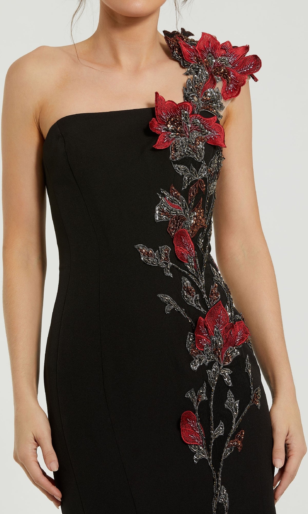 A woman wears the Mac Duggal 11779 one-shoulder black formal dress, featuring intricate red and silver floral appliqué detailing along the side and shoulder.